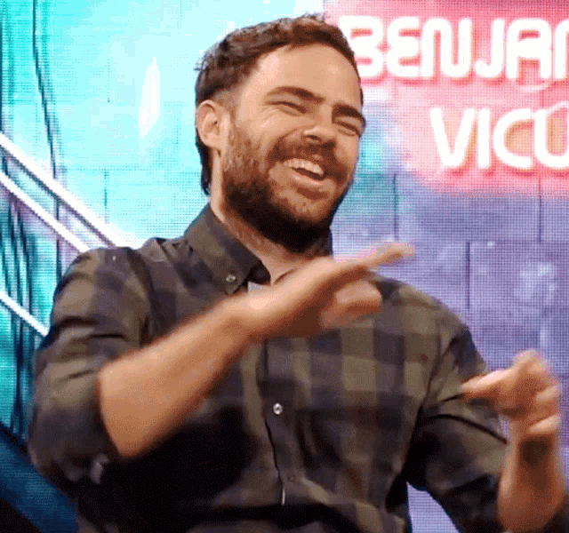 a man in a plaid shirt laughs in front of a sign that says benjac vicu