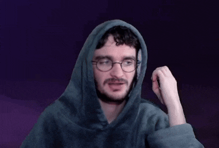 a man with a beard and glasses is wearing a hoodie and holding his fist up .