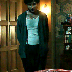 a man wearing a green cardigan and a white tank top is standing in a dark room