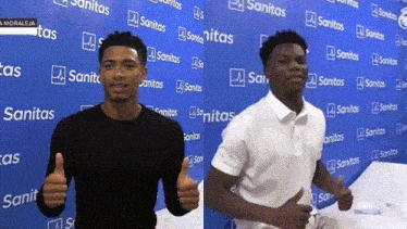 two men are giving a thumbs up in front of a wall with sanitas written on it
