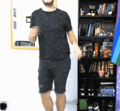 a man in a black shirt and shorts is dancing in front of a bookshelf .