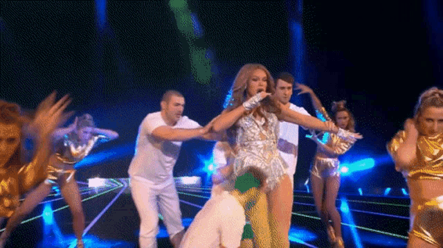 a group of people are dancing on a stage with a woman in a silver outfit