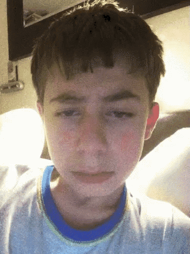 a young boy is making a sad face and has a blue shirt on