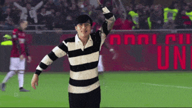 a man in a black and white striped shirt stands on a soccer field in front of a sign that says uni