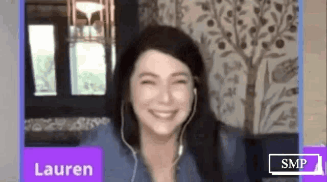 a woman is smiling while wearing headphones while sitting in front of a window .