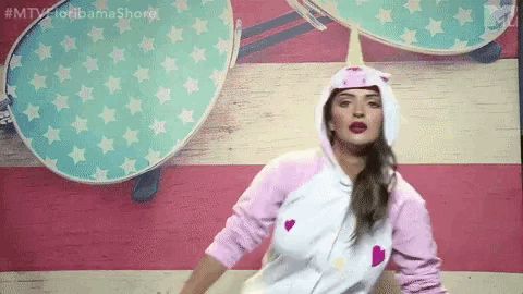 a woman in a unicorn costume is dancing in front of a pink and white american flag .