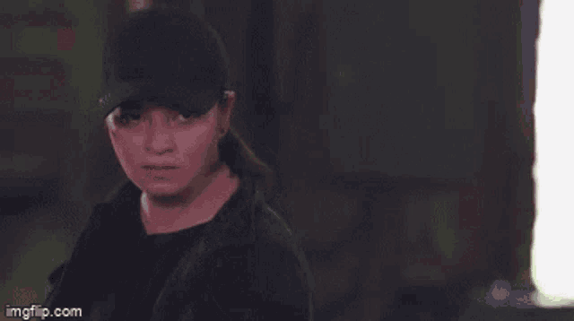 a woman wearing a black hat and a black jacket is giving the middle finger .