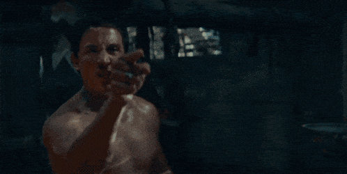 a shirtless man is standing in a dark room with a bucket in the background