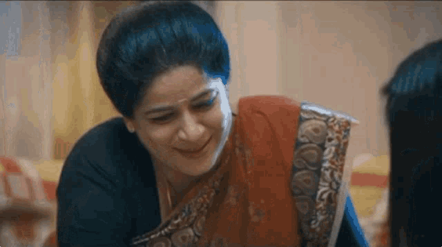 a woman in a sari is smiling and talking to another woman while sitting on a couch .