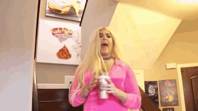 a woman in a pink wig is holding a cup of coffee .