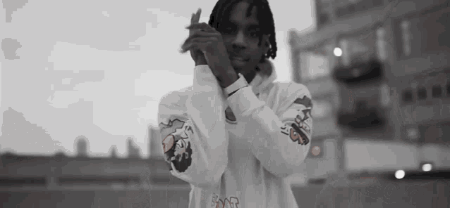 a man wearing a white hoodie with a dragon on the sleeves holds his hands together