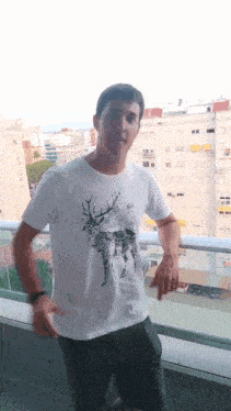a man is standing on a balcony wearing a white shirt with a deer on it