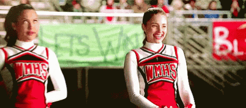 two cheerleaders wearing wmhs uniforms are standing in front of a banner