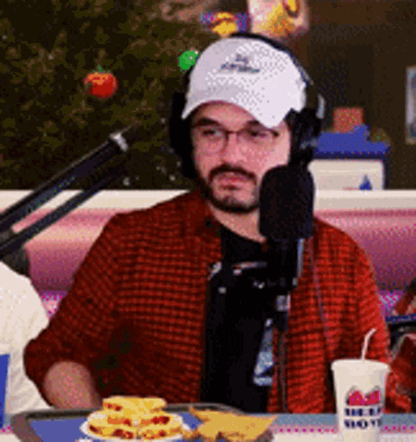 a man wearing headphones and a hat is sitting at a table in front of a microphone ..
