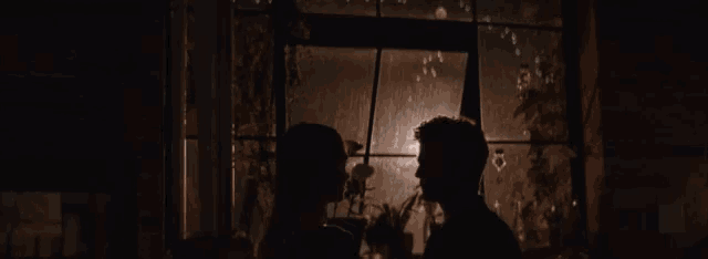 a man and a woman are standing in front of a window at night