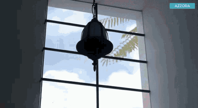 a bell is hanging from the ceiling in front of a window with azzora in the corner