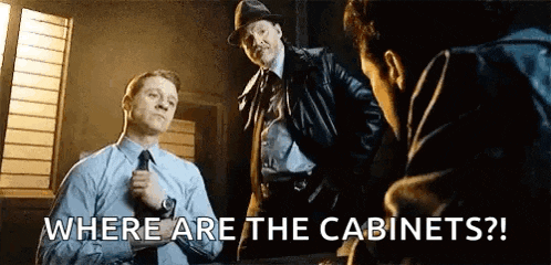 a group of men are standing around a table talking to each other and one of them is asking where are the cabinets ?
