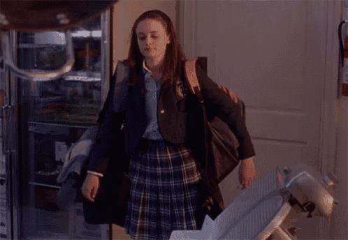 a woman in a plaid skirt is standing in front of a door with a backpack on her back .