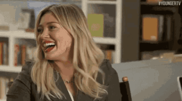 a woman in a suit is sitting in a chair and laughing .
