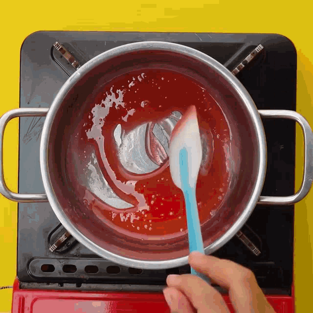 a person is stirring a red liquid with a spatula in a pot