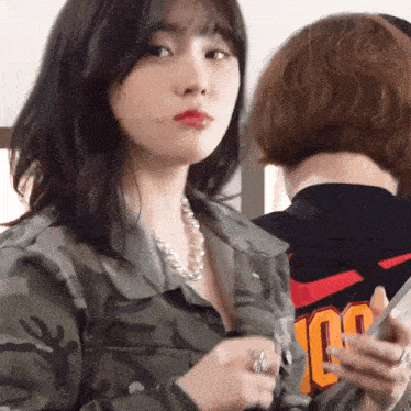a woman wearing a camouflage jacket and a necklace has the number 100 on her back