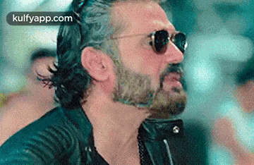 a man with a beard wearing sunglasses and a leather jacket is making a funny face .