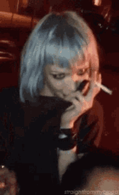 a woman with blue hair is smoking a cigarette .