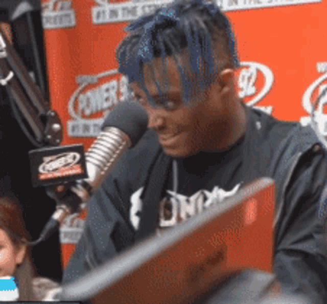 a man with blue hair is sitting in front of a microphone with the number 92 in the background