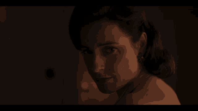 a woman without a shirt is looking over her shoulder in a dark room