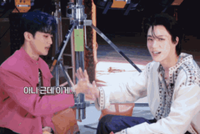 two men are sitting next to each other and one of them is wearing a pink jacket and the other is wearing a white shirt