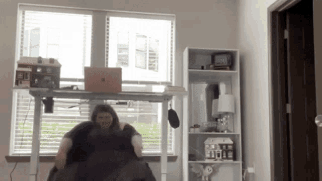 a woman is sitting at a desk with a laptop and a clock that says 10:08