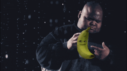 a man in a black sweatshirt holds a banana with a face on it