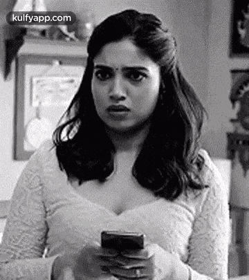 a woman is holding a cell phone in her hand and looking at it .