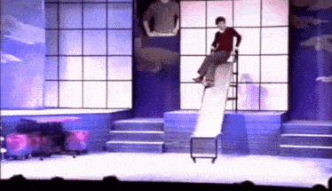 a man is sitting on a slide on stage