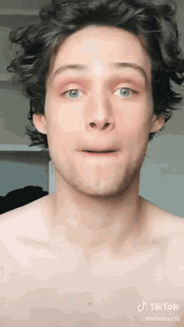 a young man without a shirt is making a funny face while looking at the camera .