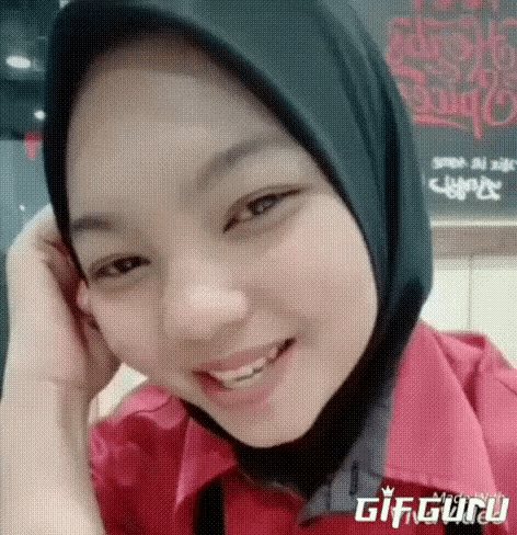 a woman wearing a hijab and a red shirt is smiling for the camera