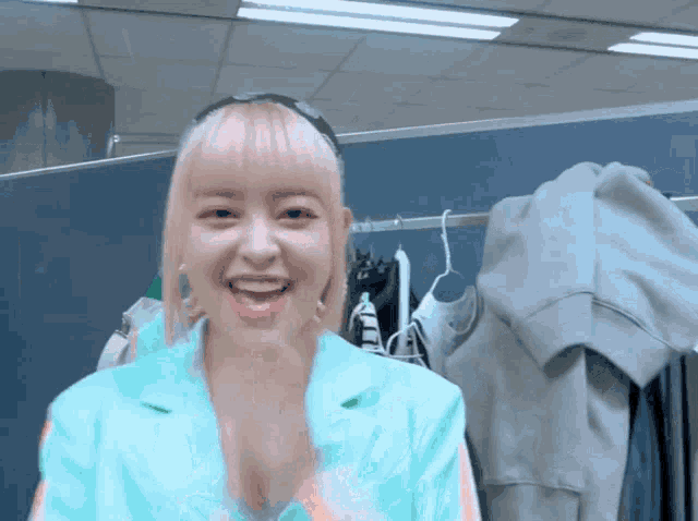 a woman with pink hair is smiling in front of a clothes rack
