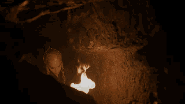 a woman is standing in a dark cave holding a fire
