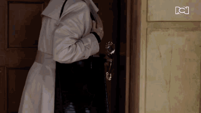 a woman in a trench coat is standing in front of a door
