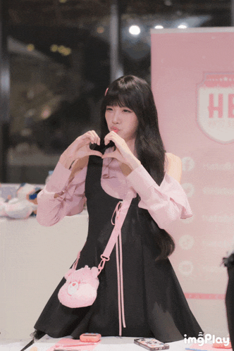 a girl in a black dress making a heart with her hands
