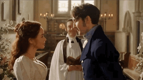 a man and a woman are standing next to each other in a church with a priest standing behind them .