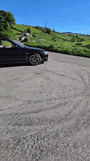 a black car is parked in a parking lot with a field in the background