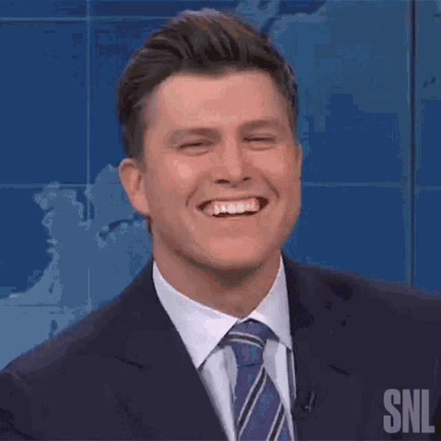 a man in a suit and tie is smiling with a snl logo in the background .