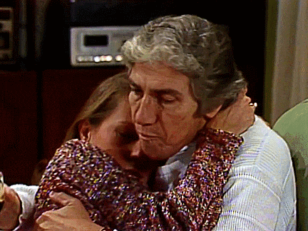 a man and a woman hugging each other with a clock in the background