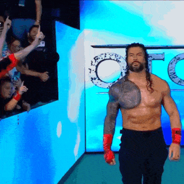 a shirtless wrestler with a tattoo on his chest walks into a room with a sign that says o