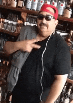 a man wearing a red hat and sunglasses is standing in front of a shelf of liquor .