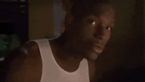 a man wearing a white tank top is looking at the camera .