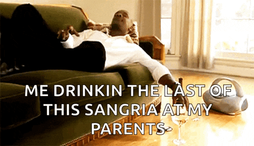 a man is laying on a couch holding a bottle of sangria and a glass of wine