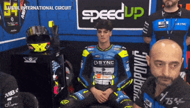 a man in a speed up motorcycle suit sits in a corner