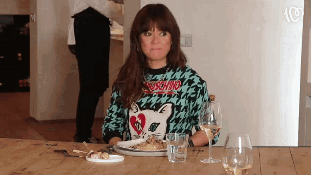 a woman wearing a moschino shirt sits at a table